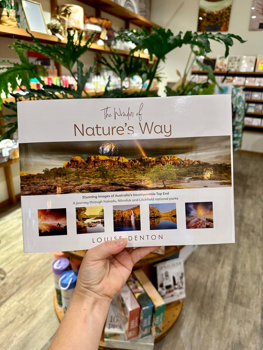A hand holding a hard-cover coffee table book titled 'The Wonder of Nature's Way' by Louise Denton, showcasing photography from the Top End of Australia.